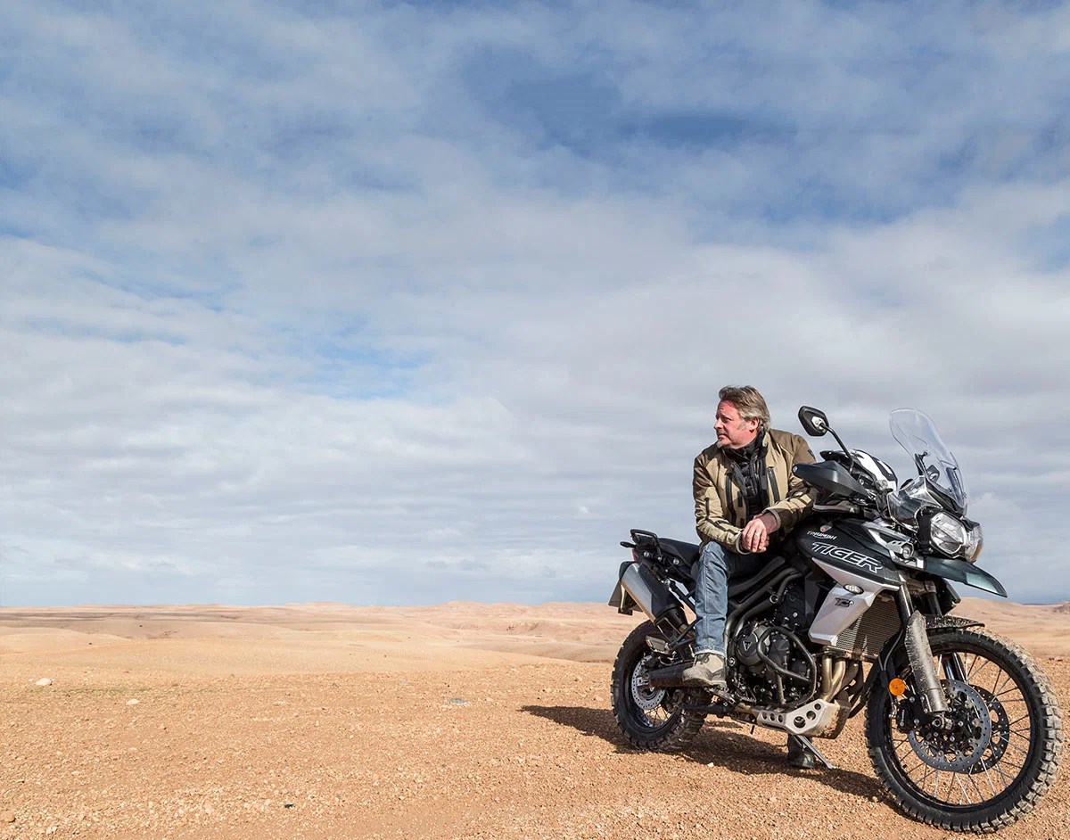 Charley Boorman assis sur une moto Triumph Tiger.